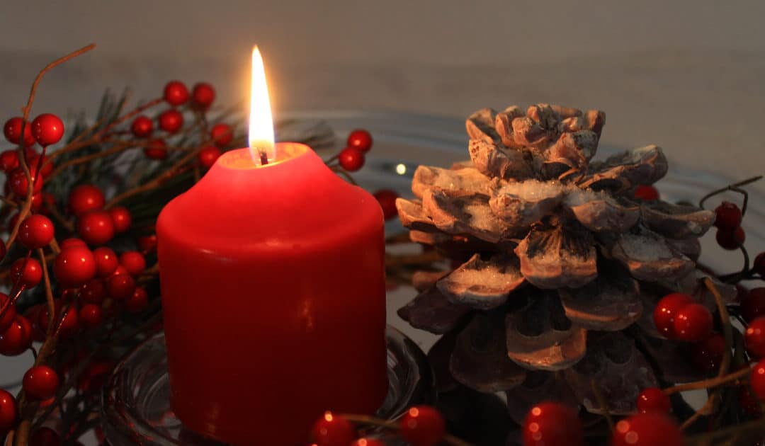 a christmas candle with frosted pine cones and red berries