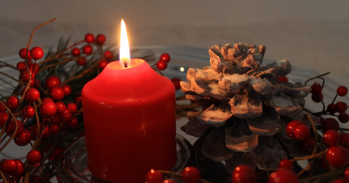 a christmas candle with frosted pine cones and red berries